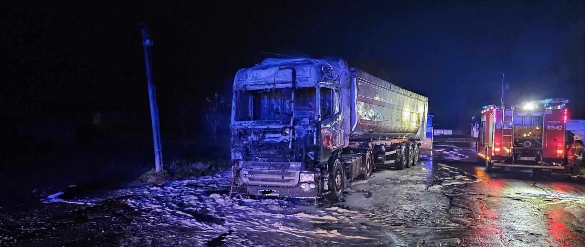 Zdjęcie przedstawia spalony samochód ciężarowy, po prawej stronie widać tył wozu strażackiego 