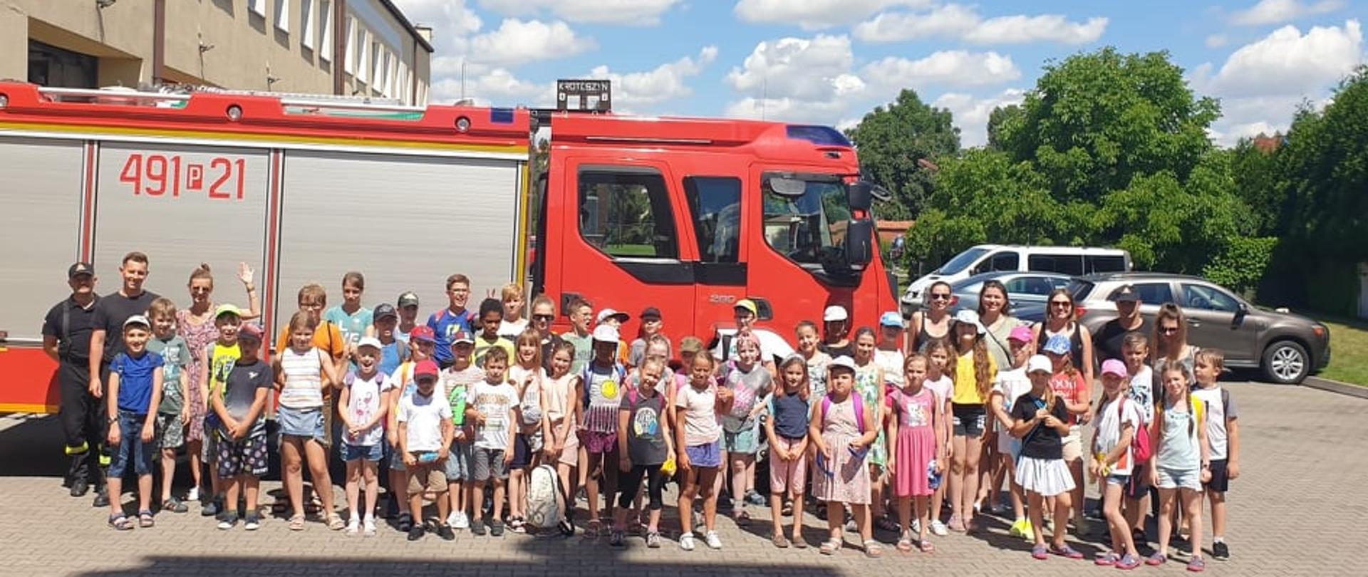 Zdjęcie grupowe na tle pojazdu pożarniczego. Na zdjęciu dzieci z półkolonii, opiekunowie oraz strażacy. 