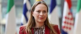 Minister funduszy i polityki regionalnej Katarzyna Pełczyńska-Nałęcz idzie korytarzem, za jej plecami flagi państw członkowskich UE
