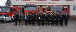 Strażacy z KP PSP i JRG w Miechowie w umundurowaniu na tle samochodów pożarniczych oraz budynku JRG.