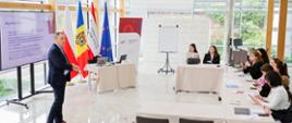 Grupa kobiet słucha mężczyzny, który stoi obok ekranu z wyświetloną prezentacją i prowadzi szkolenie
