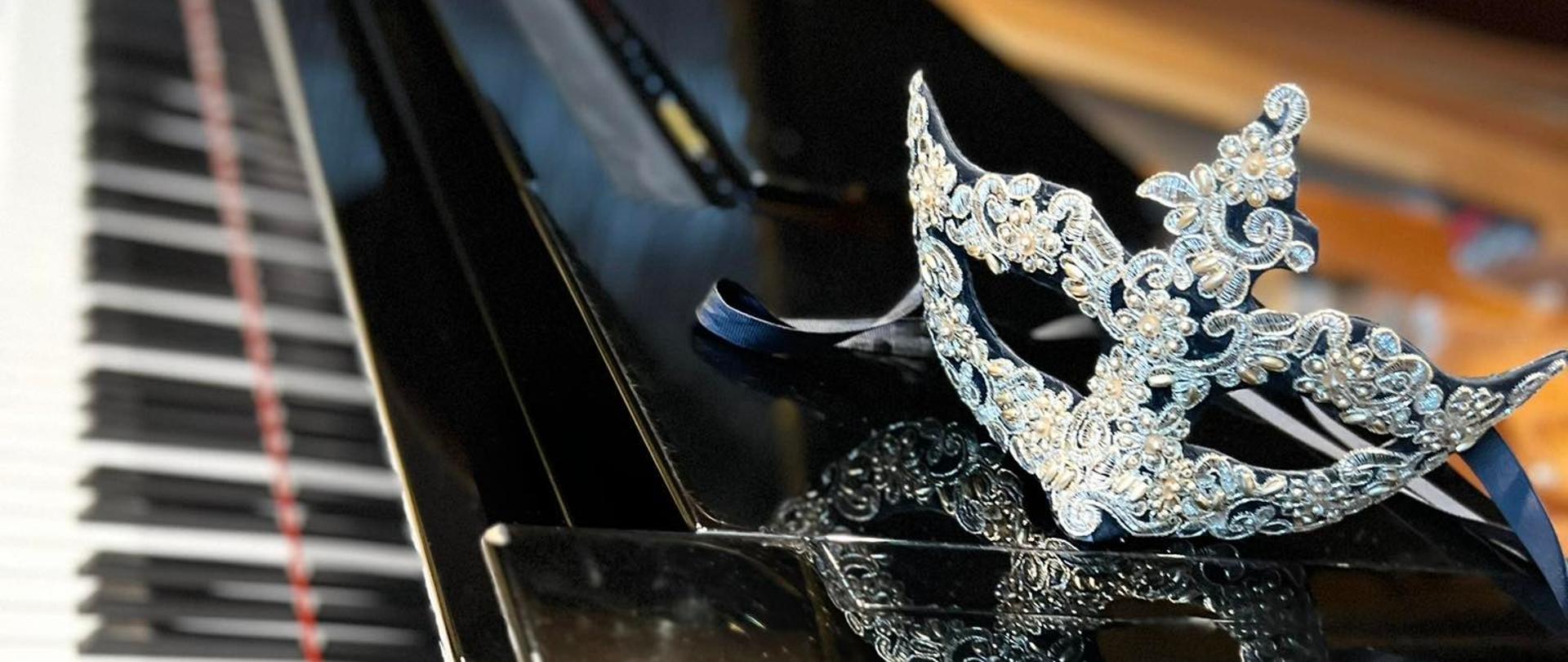 Na plakacie czarny fortepian a na nim maska karnawałowa ozdobiona białymi perełkami