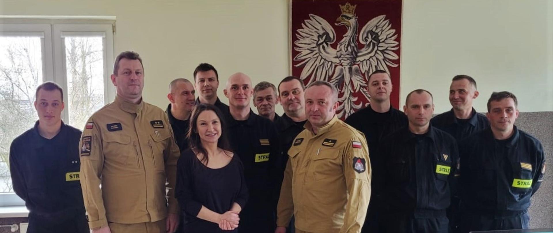 Na zdjęciu Komendant Miejski Państwowej Straży Pożarnej w Częstochowie wraz z Dowódcą Jednostki Ratowniczo – Gaśniczej numer 1 w Częstochowie, Panią Martą oraz strażakami Jednostki Ratowniczo – Gaśniczej numer 1 w Częstochowie. W tle Godło Państwowe.