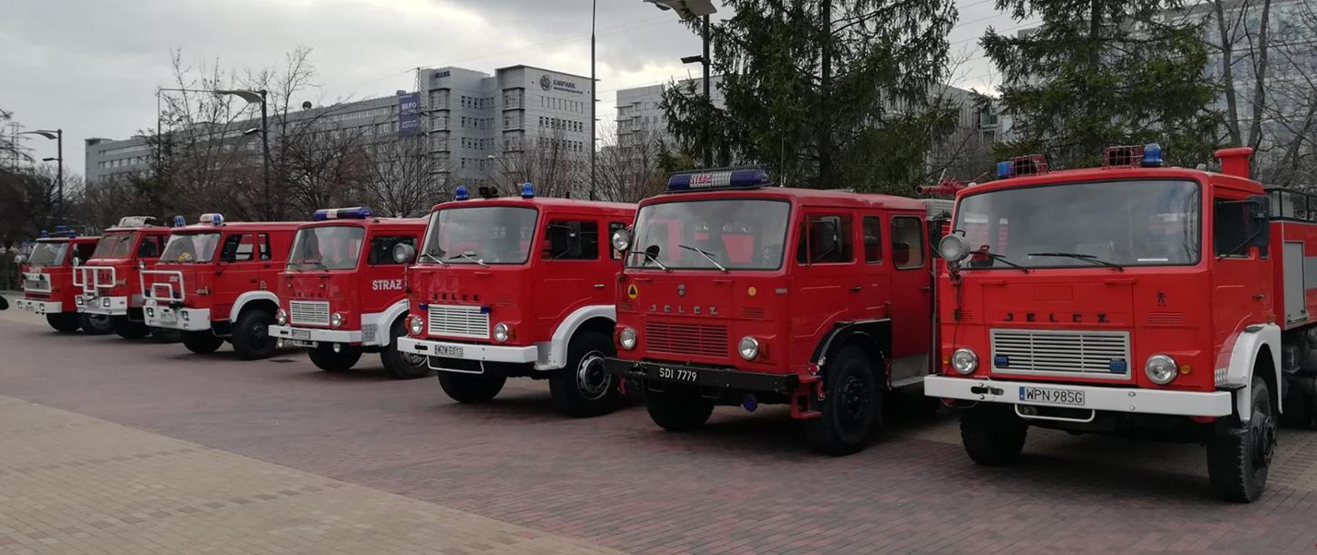 7 samochodów pożarniczych ustawionych koło siebie, w tle widac bloki