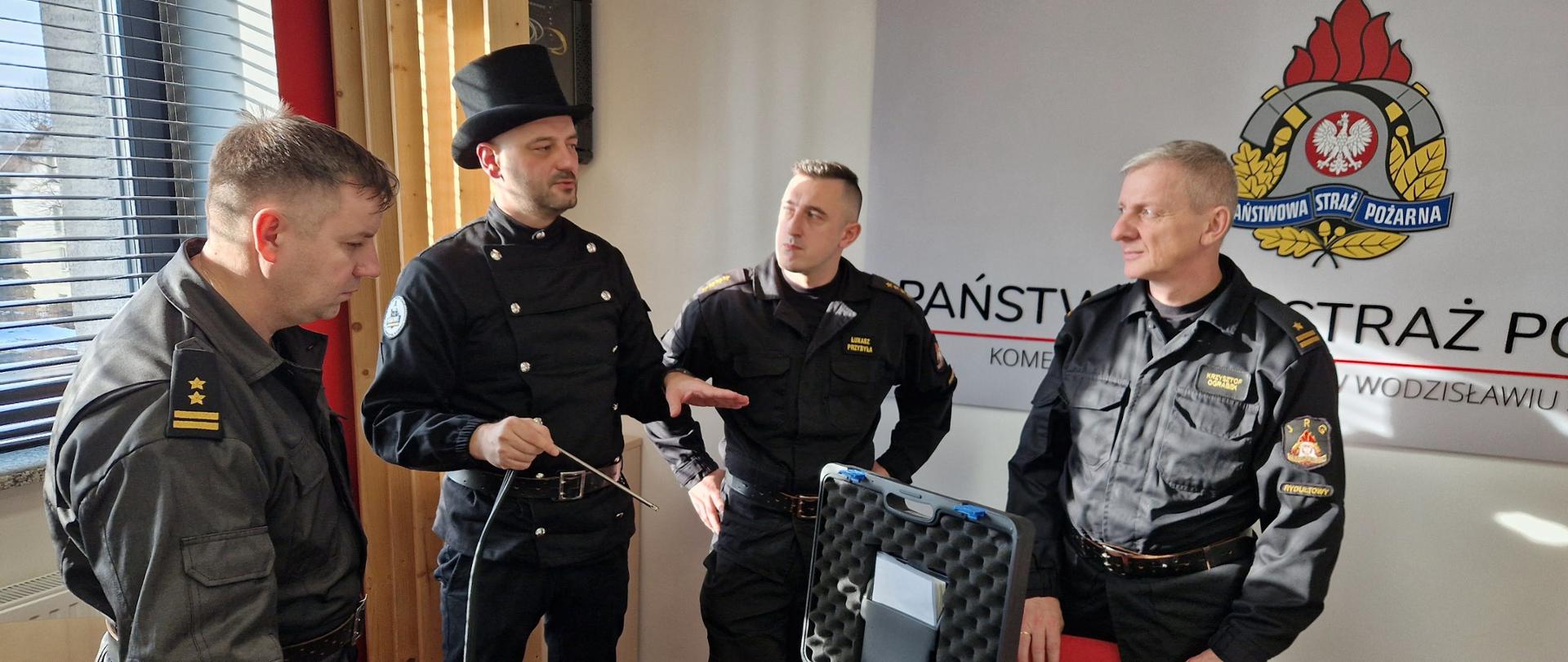 Na zdjęciu trzech strażaków PSP oraz mistrz kominiarski podczas wspólnego spotkania. W tle logo Państwowej Straży Pożarnej.
