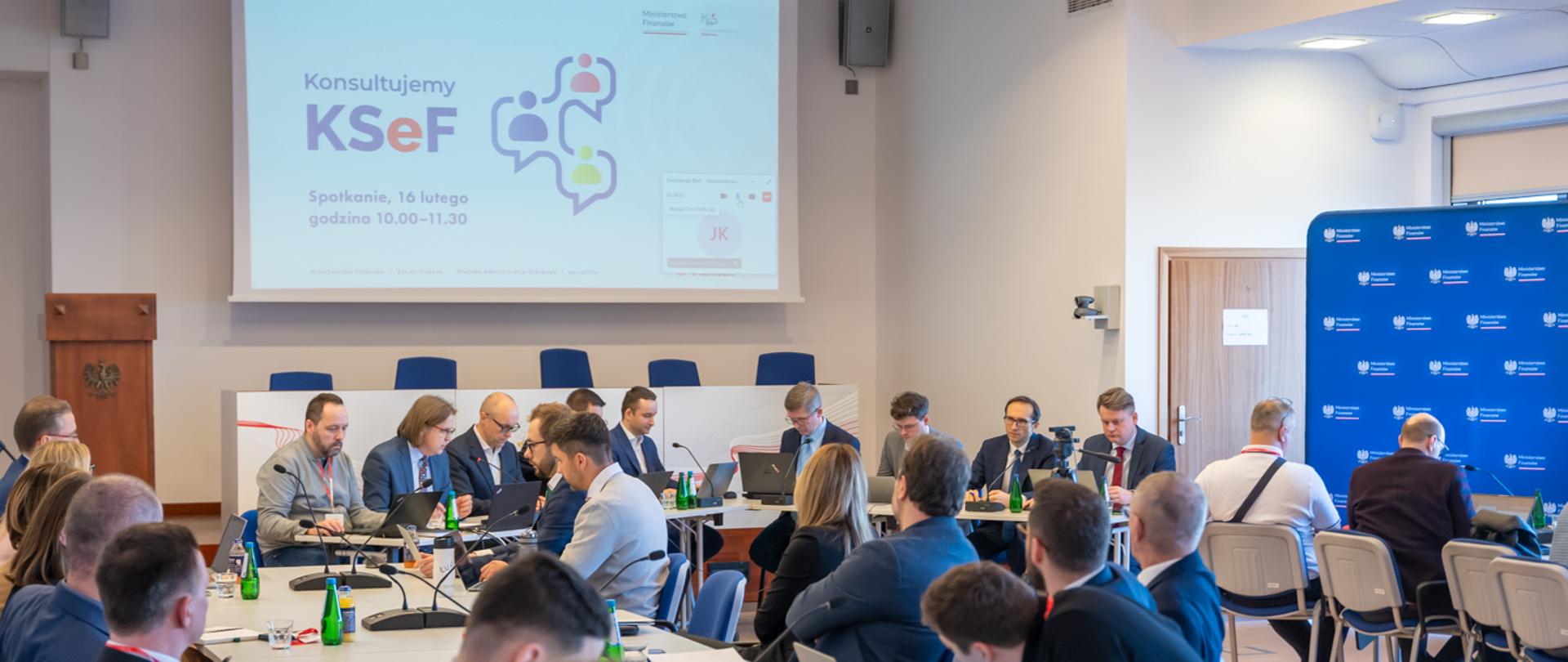 Kilkanaście osób siedzących przy stole podczas konsultacji.