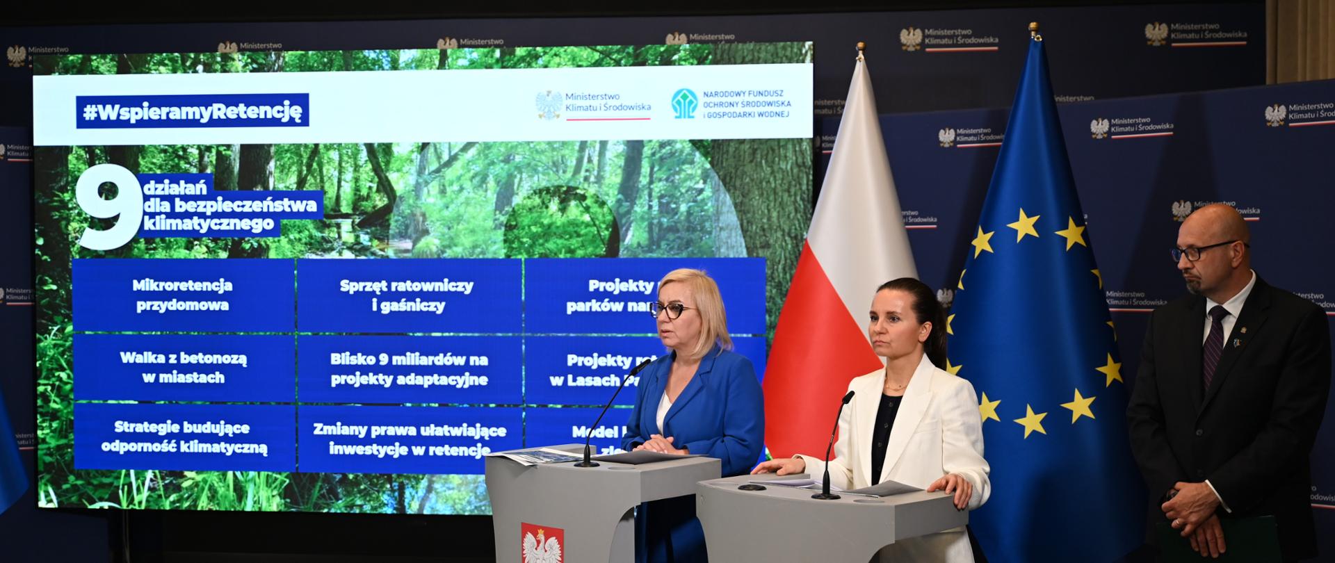 Ministra klimatu i środowiska Paulina Hennig-Kloska, wiceministra Urszula Zielińska i zastępca prezesa zarządu NFOŚiGW Robert Gajda podczas konferencji prasowej nt. pakietu 9 działań wzmacniających bezpieczeństwo klimatyczne Polski, która odbyła się 24 czerwca 2026 r. w Warszawie. Ministry stoją obok siebie przy mównicach, a obok nich, po prawej stronie stoi zastępca prezesa. W tle od prawej widać flagę UE, flagę Polski oraz ekran z prezentacją, na którym jest wymienione 9 działań dla bezpieczeństwa klimatycznego.