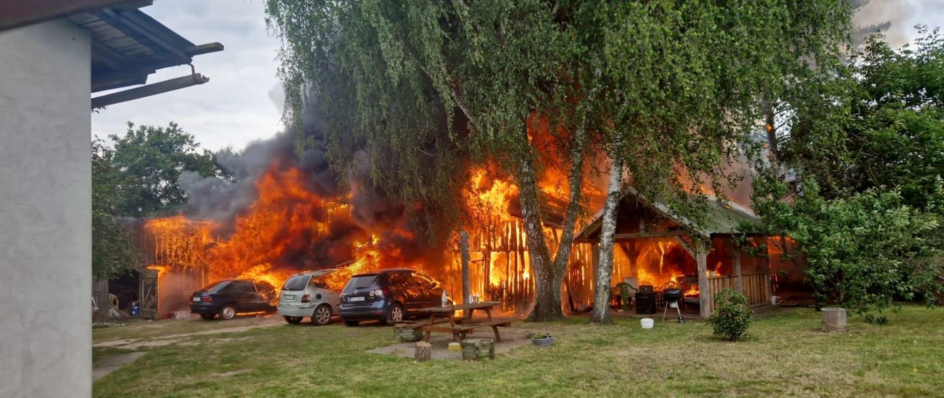 budynek gospodarczy objęty pożarem, przed nim stoją 3 auta osobowe również w ogniu