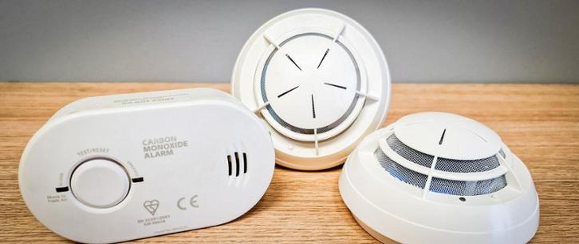 Czujniki wykrywające obecność tlenku węgla oraz dymu leżą na drewnianym podłożu.