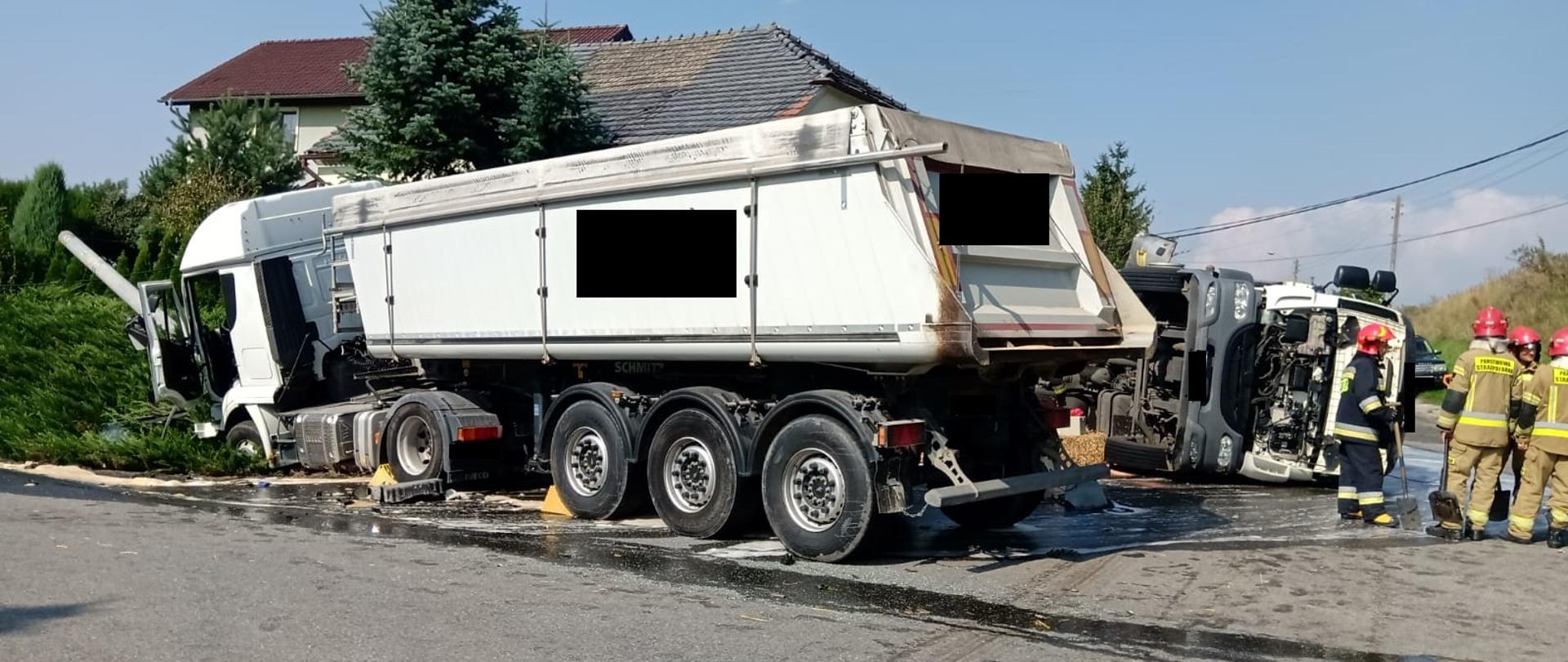 Zdjęcie przedstawia miejsce zdarzenia po wypadku samochodów ciężarowych. Po prawej stronie strażacy w mundurach bojowych