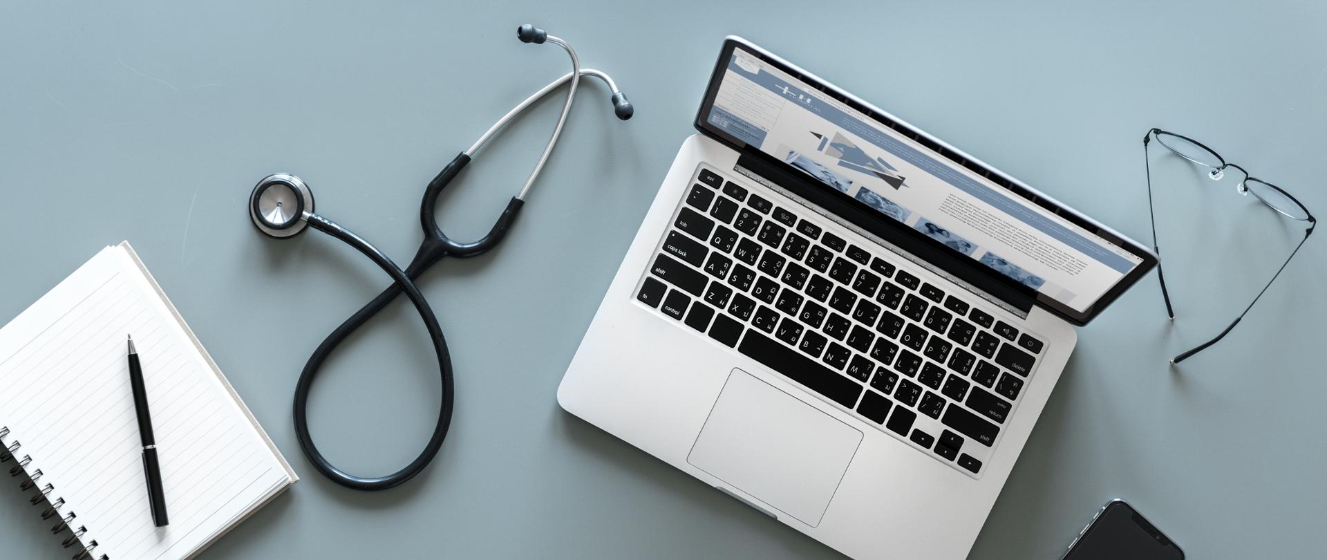 Zdjęcie przedstawia stetoskop. Obok niego laptop i notes.