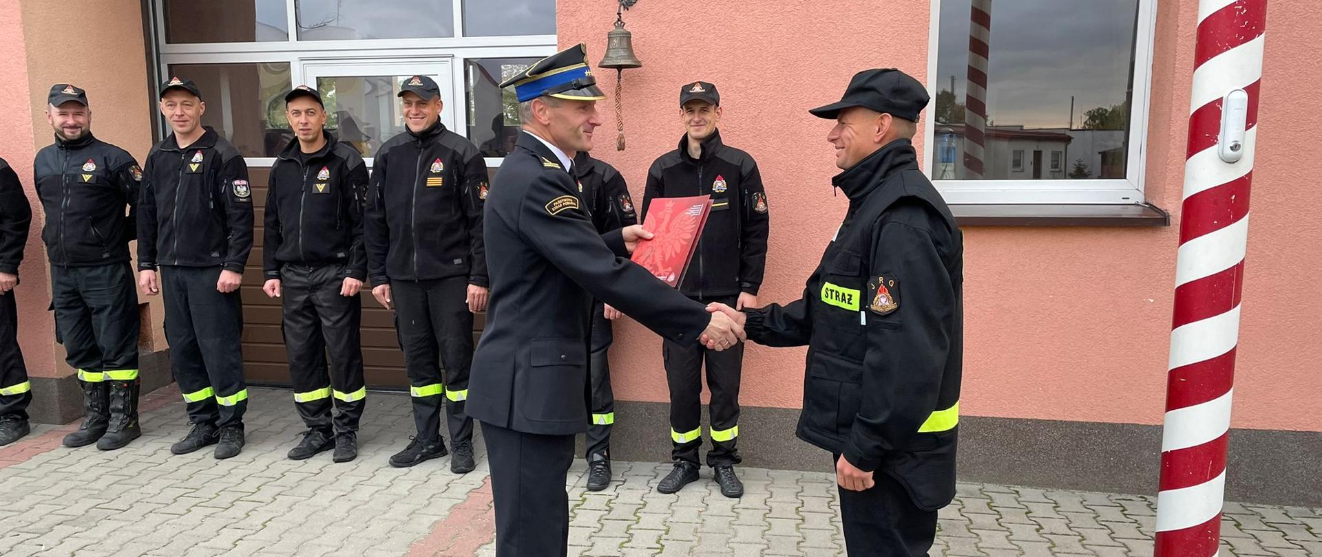 Zdjęcie przestawia wręczenie aktu ślubowania przez komendanta powiatowego państwowej straży pożarnej nowo przyjętego strażaka.