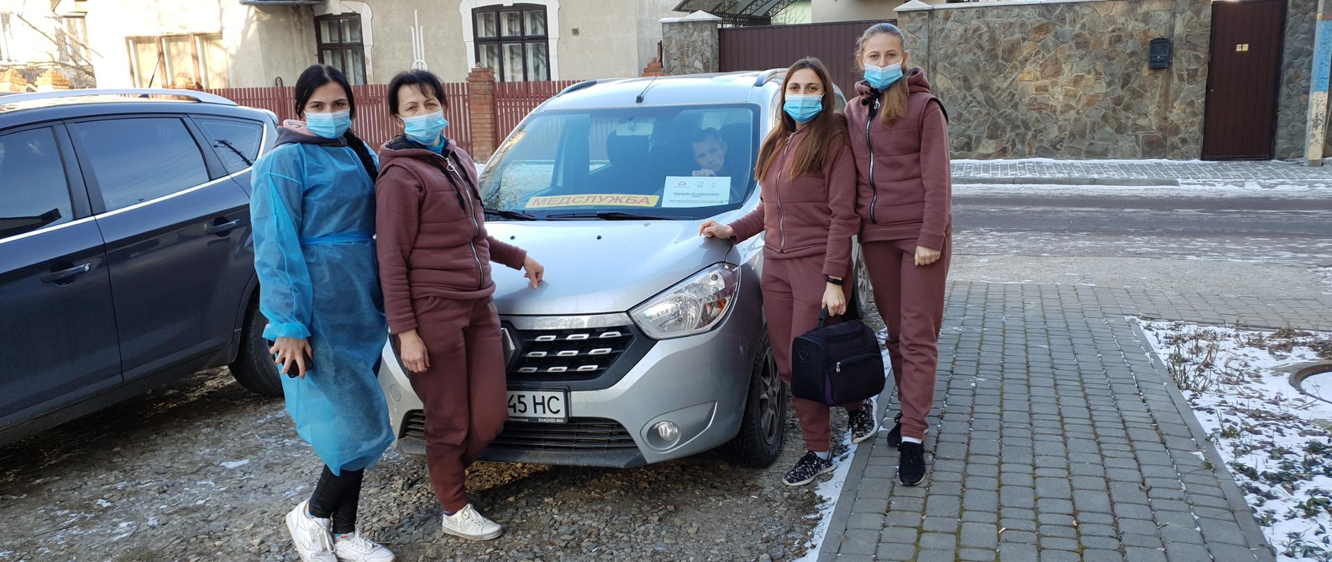 Cztery kobiety w maseczkach stoją obok samochodu.