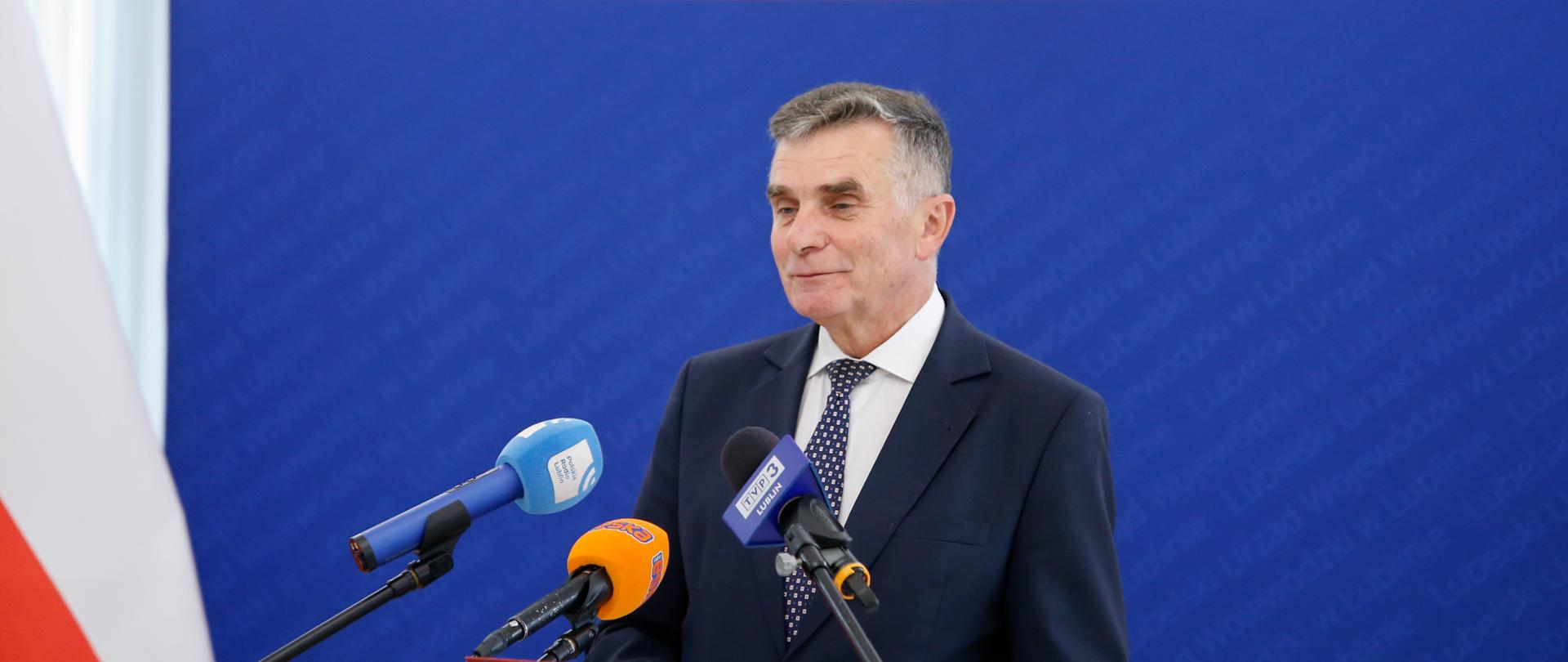Wojewoda lubelski stoi na tle niebieskiej ścianki z napisem Lubelski Urząd Wojewódzki w Lublinie.