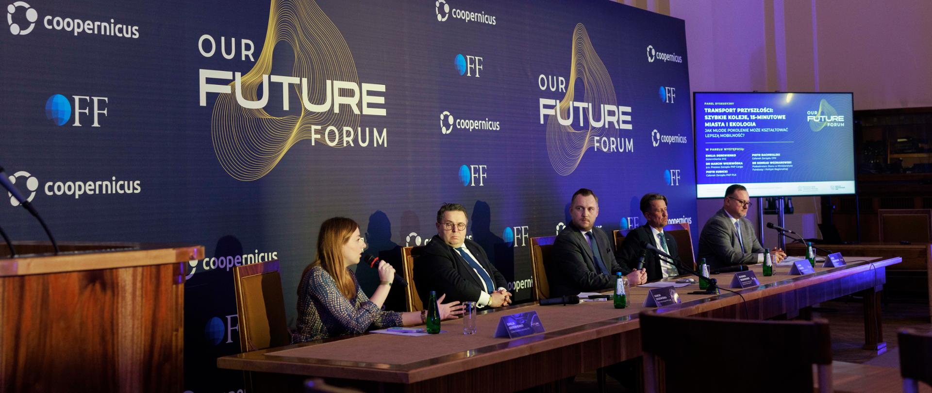 Wiceminister Konrad Wojnarowski wśród uczestników debaty podczas Our Future Forum, którzy siedzą przy stole na tle ścianki