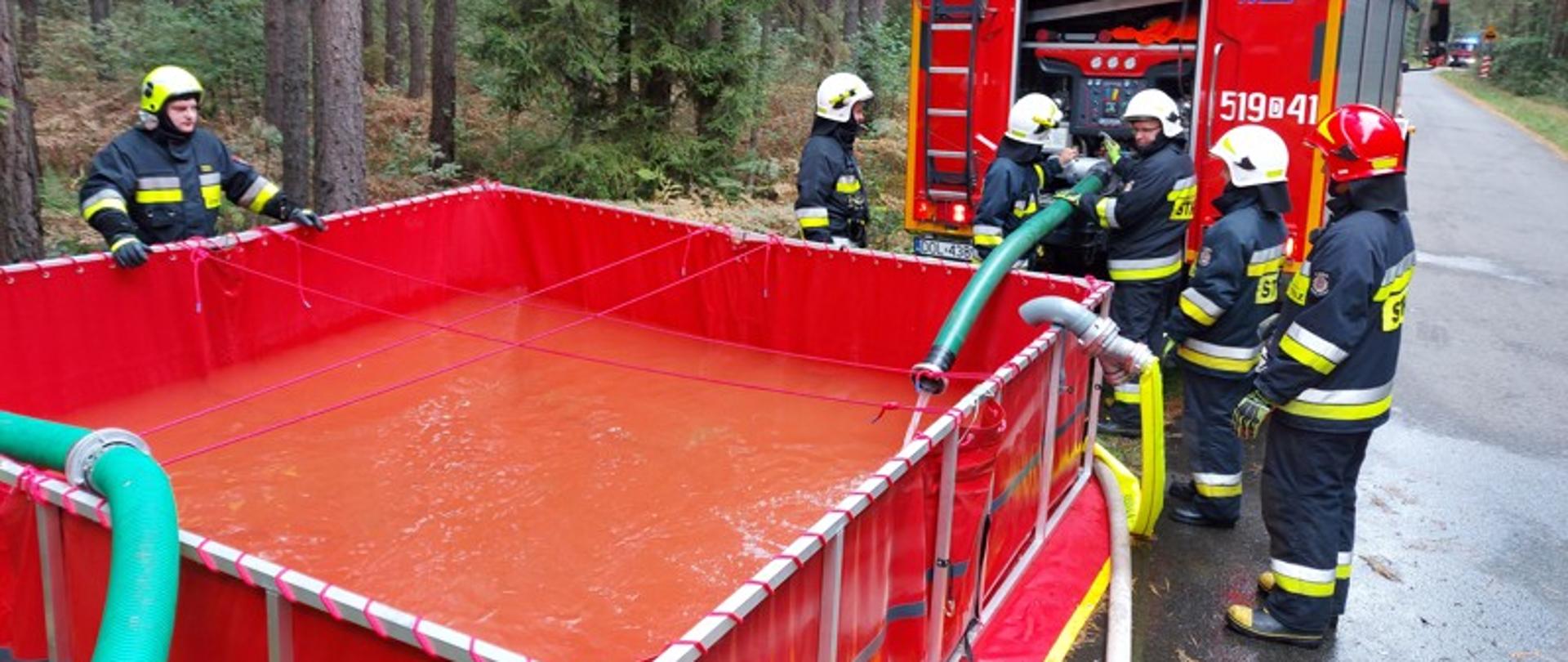 Na zdjęciu widać strażaków w czasie dokonywaniu zrzutu wody do zbiornika. 