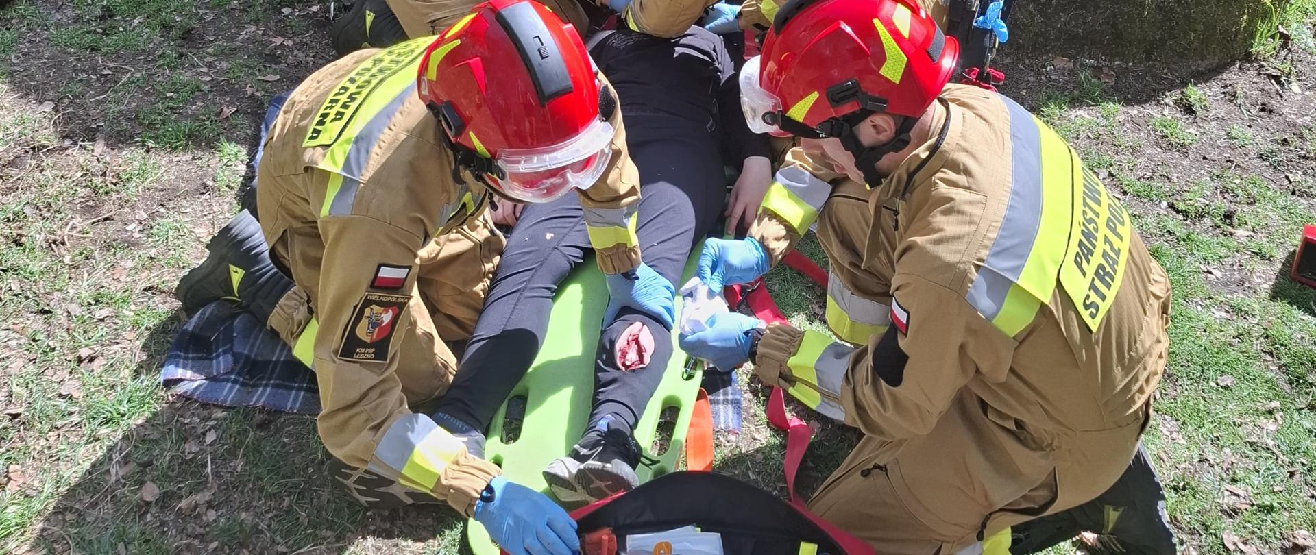 Strażacy opatrują osobę poszkodowaną leżącą na noszach.