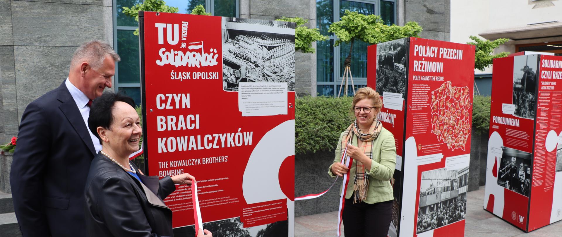 Na zdjęciu znajdują się dwie kobiety oraz mężczyzna odsłaniający wystawę 