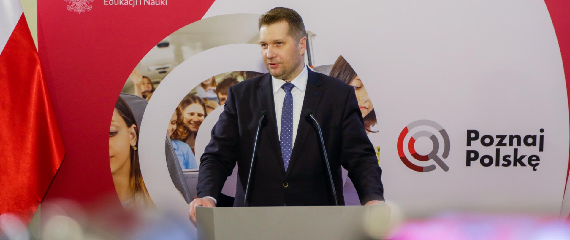Minister Przemysław Czarnek przemawia podczas konferencji, stoi przed mównicą, za nim stoi baner z napisem Poznaj Polskę.