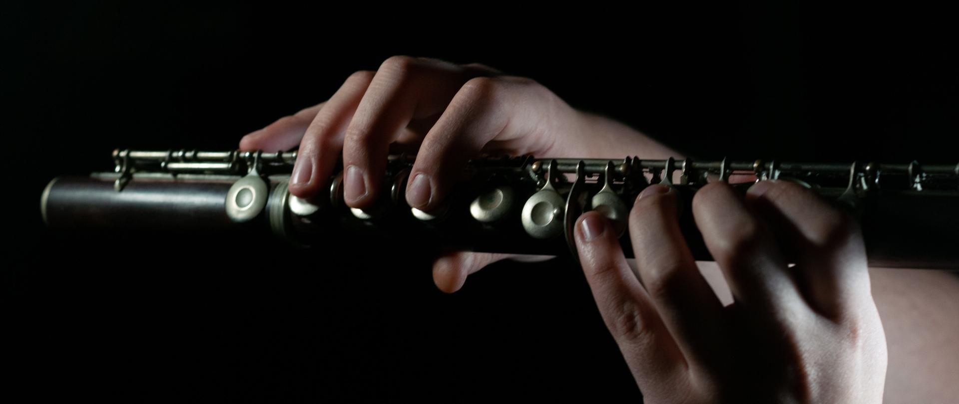 w centralnej części dłonie trzymają obój, całość na czarnym tle