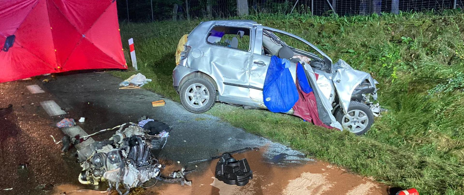 Zdjęcie przedstawia rozbite auto. silnik z auta lezy na drodze.