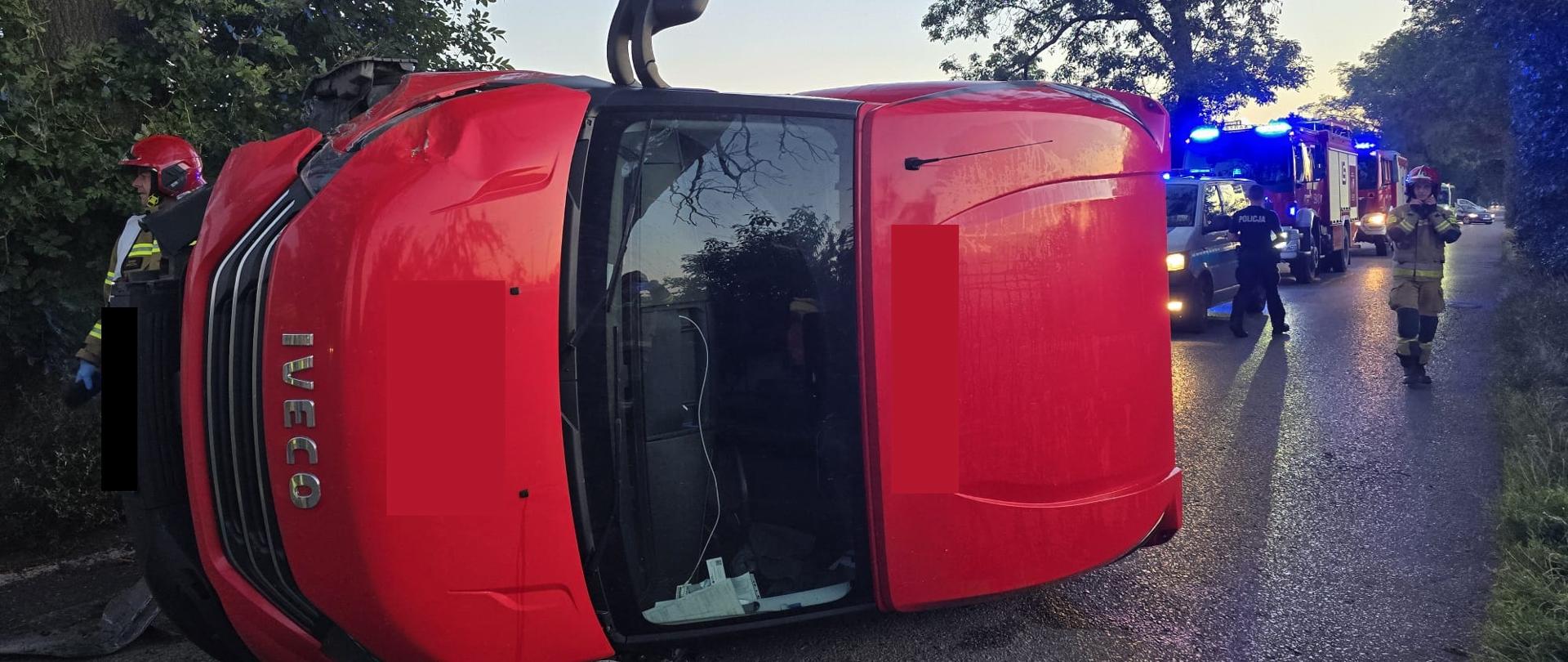 Pojazd leży na drodze, w pobliżu strażacy i policja