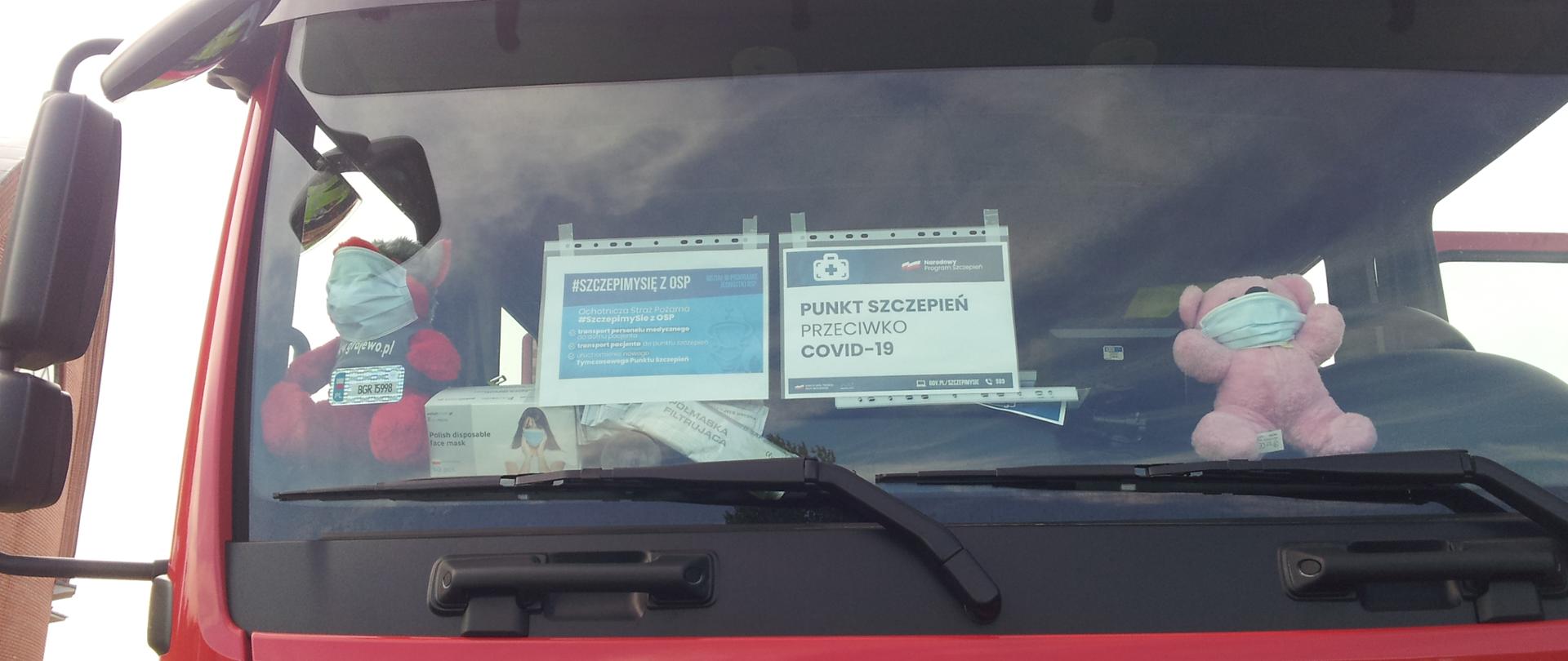 Przednia szyba pojazdu strażackiego a na niej przyklejone informacje odnośnie punktu szczepień.