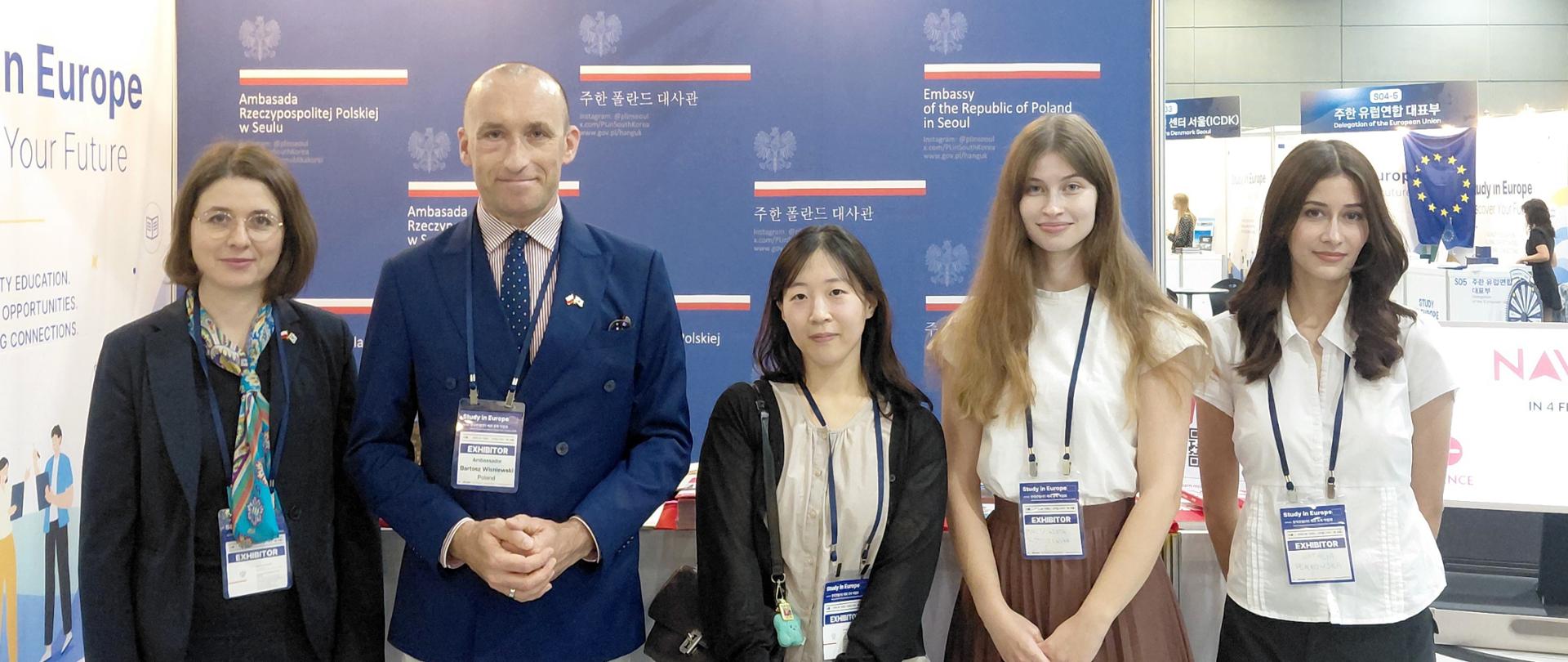 Pięć osób stoi na tle banneru z logo Ambasady RP w Seulu