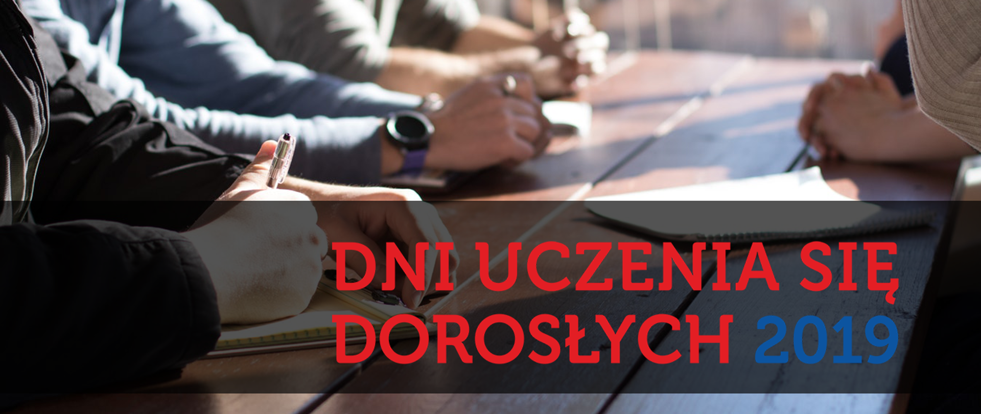 Na zdjęciu przy stole siedzą ludzie, rozmawiają, notują coś. Na czarnym tle napis: Dni uczenia się dorosłych 2019