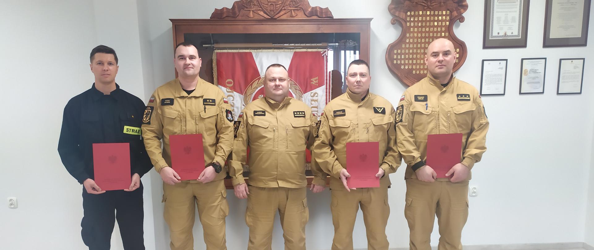 Strażacy stoją na sali sztandarowej ustawieni do zdjęcia.