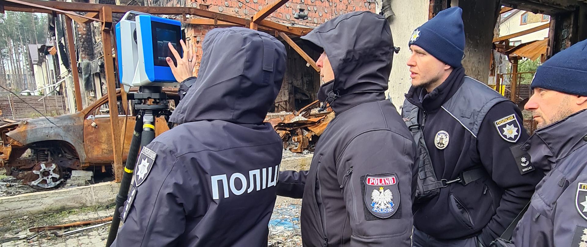 Instruktor i dwóch uczestników szkolenia przyglądają się funkcjonariuszce używającej skaner 3D do dokumentowania zniszczeń budynków