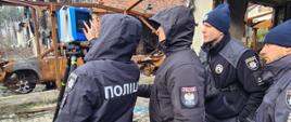 Instruktor i dwóch uczestników szkolenia przyglądają się funkcjonariuszce używającej skaner 3D do dokumentowania zniszczeń budynków