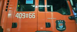 Zdjęcie przedstawia kabinę samochodu ratowniczo-gaśniczego koloru czerwonego jednostki OSP w Trzebielinie z plakatem #SzczepimySię z OSP