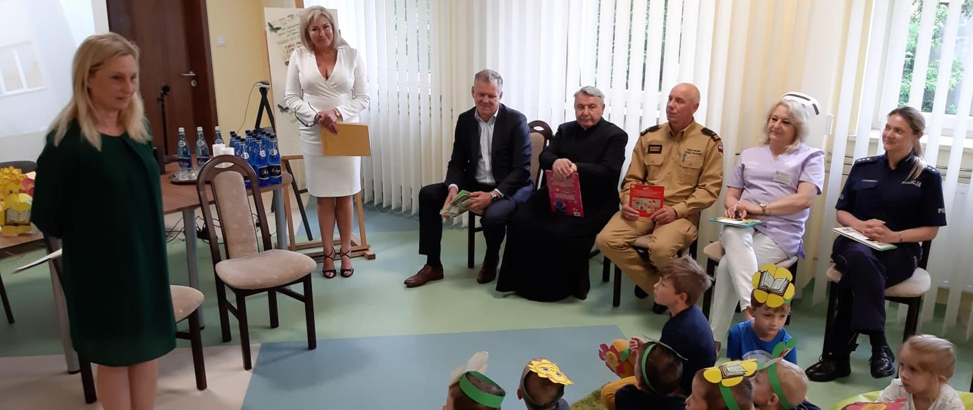 Dzieci słuchają przemówienia jednej z Pań przed czytaniem bajek przez zaproszonych gości.