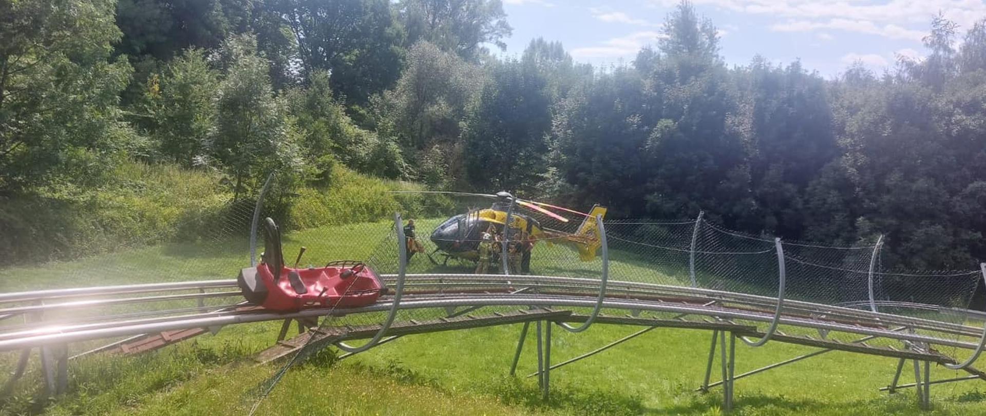 Na zdjęciu znajduje się wagonik ustawiony na zjeżdżalni grawitacyjnej, w tle stoi śmigłowiec LPR