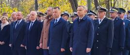Zaproszeni goście oraz przedstawiciele służb mundurowych stoją obok siebie w rzędach.