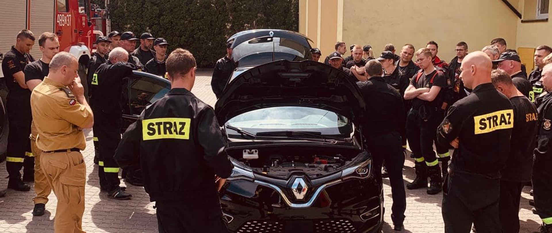 Na zdjęciu znajdują się strażacy przy samochodzie elektrycznym.