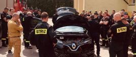 Na zdjęciu znajdują się strażacy przy samochodzie elektrycznym.