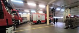 zdjęcie przedstawia zbiórkę strażaków w garażu podczas przekazania nowego pojazdu.