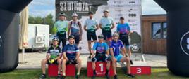 Zespół mężczyzn kolarzy na podium, uśmiechający się do kamery przed zawodami.
