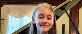 Alicja Puchalik, uczennica, siedzi na tle fortepianu w sali kameralnej Państwowej Szkoły Muzycznej I i II stopnia w Słupsku. Jest bardzo zadowolona,. Trzyma w rękach dyplom.
