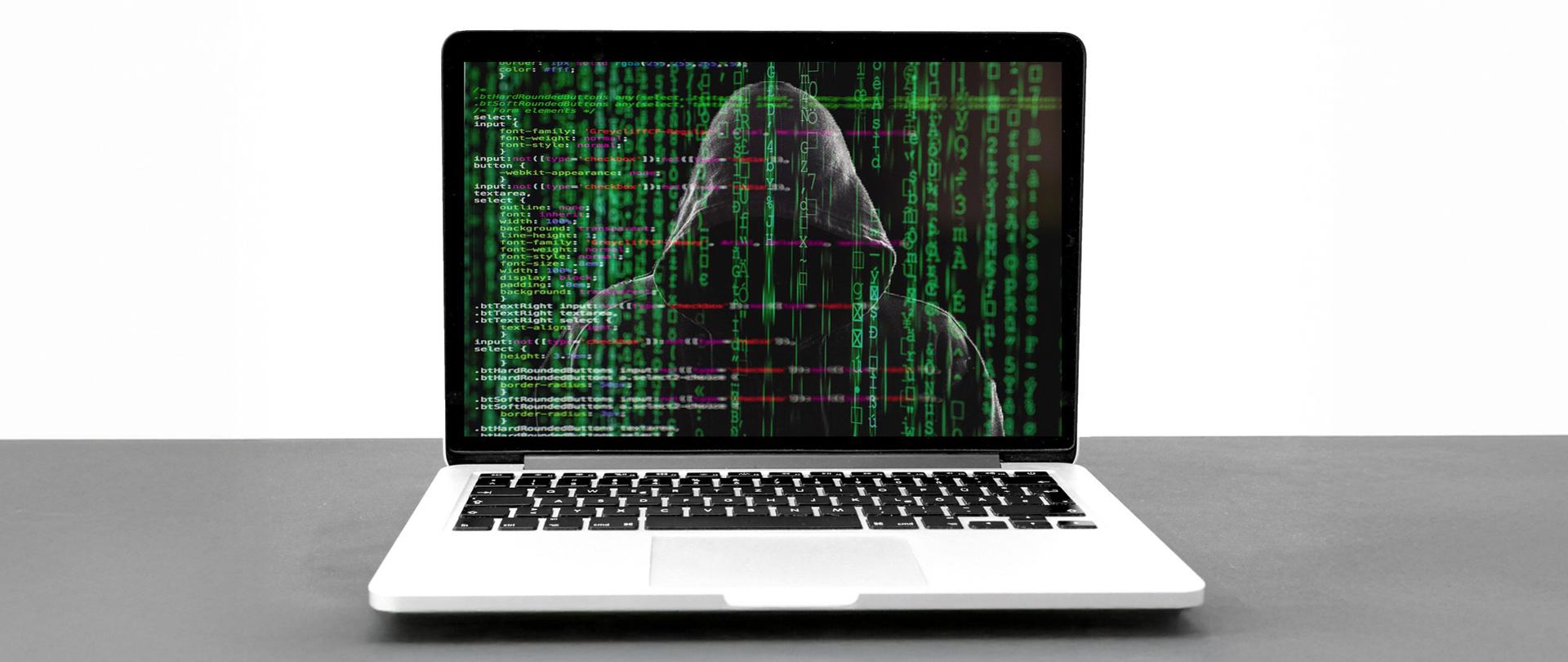 
Zdjęcie laptopa, w ekranie monitora odbija się sylwetka hakera