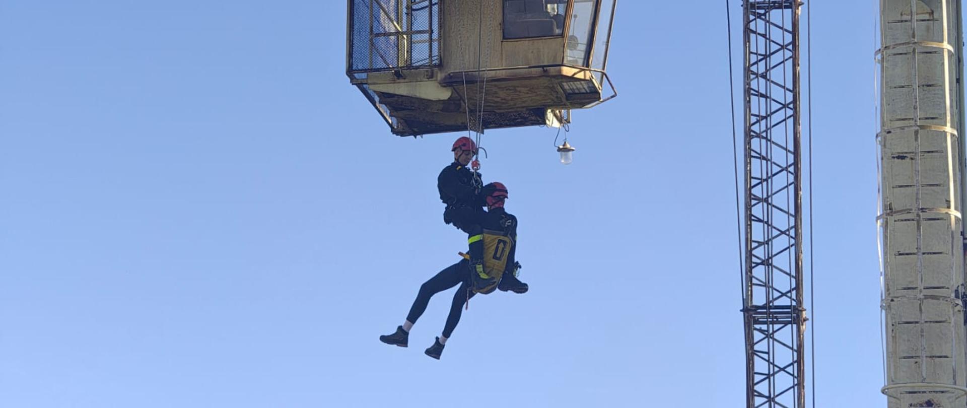 Strażak z poszkodowanym na linkach zjeżdżający w dół z suwnicy. 