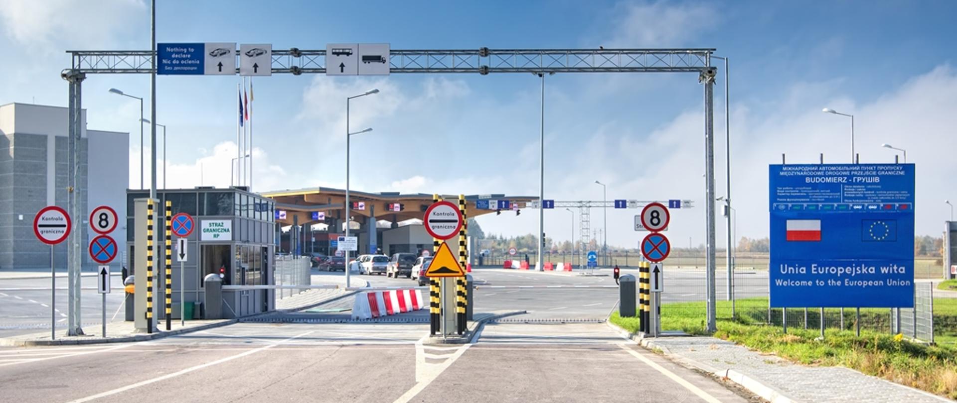 Przejście graniczne, bramki, znaki drogowe, tablica z flagą Rzeczypospolitej Polskiej i Unii Europejskiej.