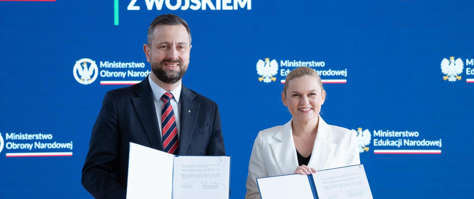 Na tle wielkiego ekranu z napisem Edukacja z wojskiem i nazwami ministerstw, stoi minister obrony narodowej Władysław Kosiniak-Kamysz oraz ministra edukacji Barbara Nowacka w rękach trzymają podpisane listy intencyjne.