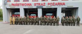Na zdjęciu widoczni są funkcjonariusze Państwowej Straży Pożarnej oraz żołnierze Wojsk Obrony Terytorialnej, stojący w szyku na tle budynku Jednostki Ratowniczo-Gaśniczej nr 2 w Ostrowcu Świętokrzyskim. 