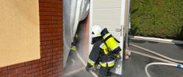 Zdjęcie przedstawia rotę strażaków w ubraniu specjalnym i SOUO oraz linią gaśniczą podczas wejścia do zadymionego pomieszczenia warsztatu JRG w Oleśnie.