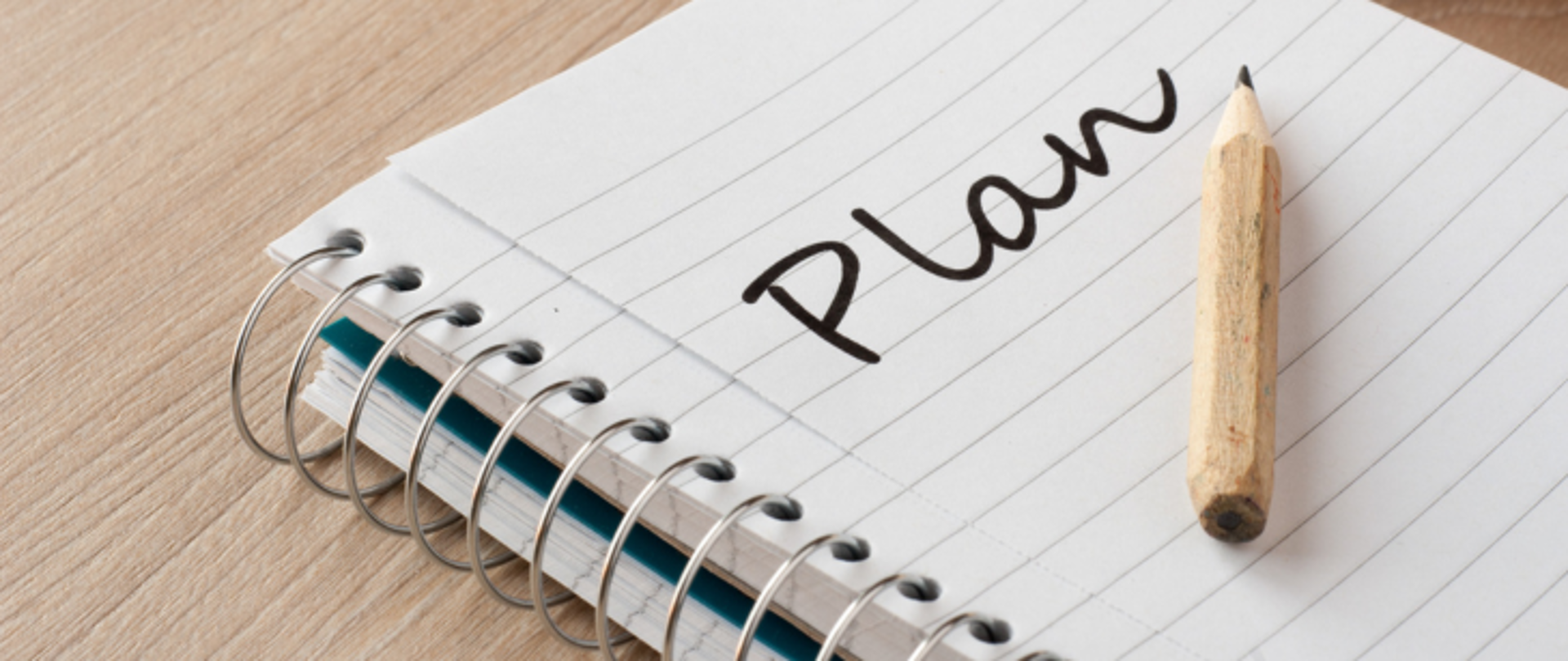 Na biurku leży zeszyt w linie. W zeszycie napis Plan. Na zeszycie leży ołówek