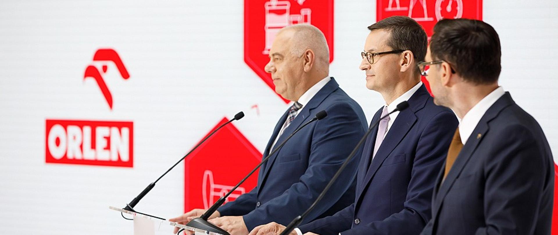 Od lewej: premier Jacek Sasin, premier Mateusz Morawiecki i Daniel Obajtek przy mównicach.