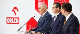 Od lewej: premier Jacek Sasin, premier Mateusz Morawiecki i Daniel Obajtek przy mównicach.